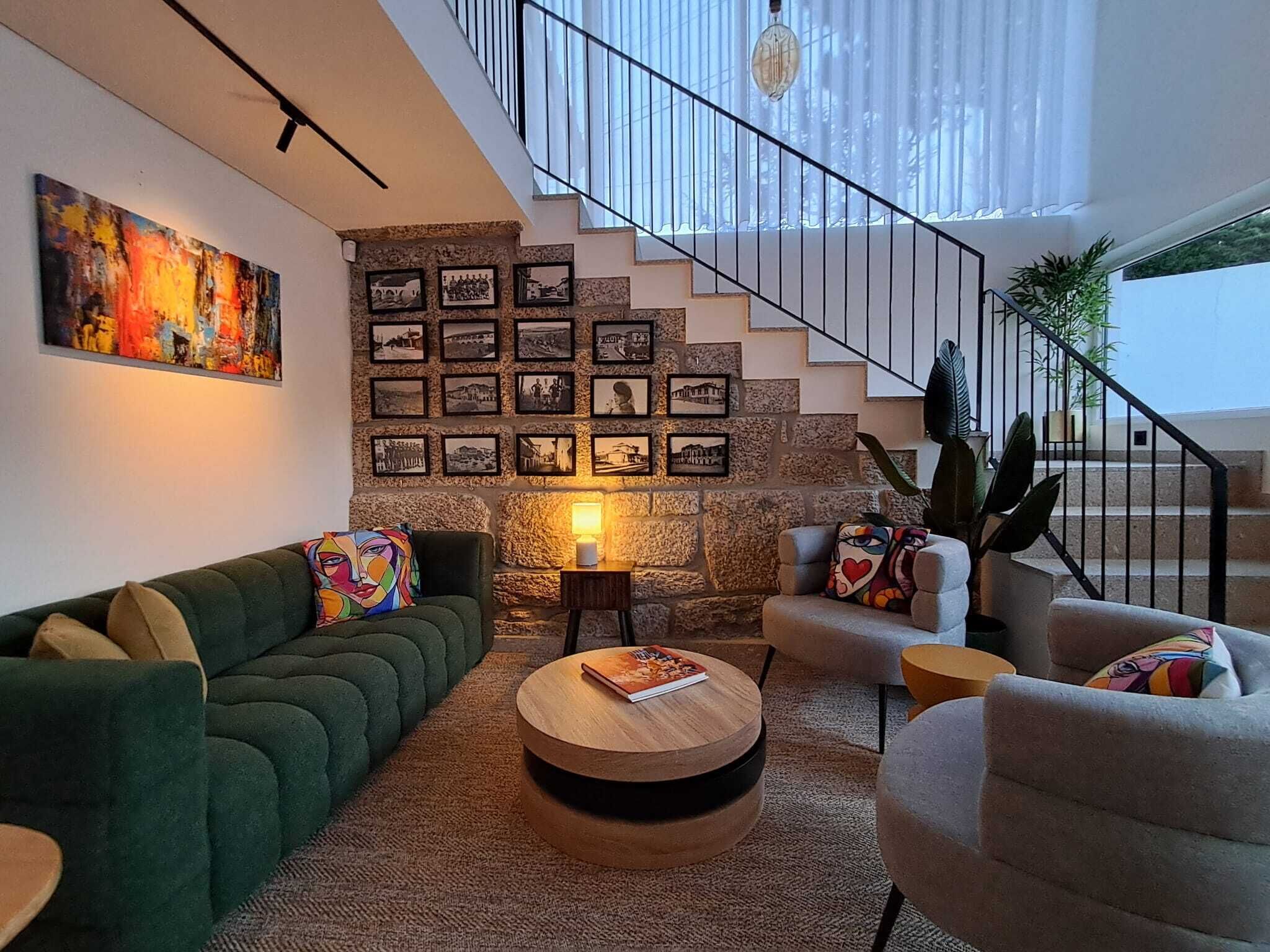 Un salon moderne avec un canapé vert, une table basse ronde et un escalier agrémenté d’un mur en pierre.