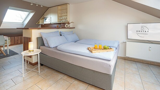Ein modernes Schlafzimmer mit Bett, Nachttisch, Lampe und einem Frühstücksbrett mit Früchten und Saft.