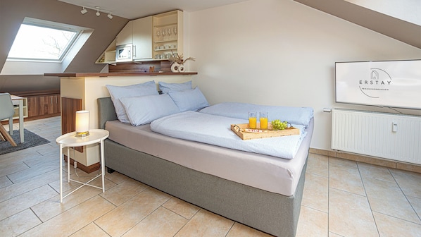 Ein modernes Schlafzimmer mit Bett, Nachttisch, Lampe und einem Frühstücksbrett mit Früchten und Saft.
