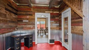Una habitación con pared de madera, un escritorio con cajones, una puerta y una ventana.