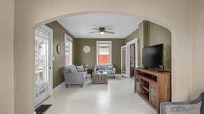 Un vaste espace de vie agrémenté d’un ventilateur de plafond, d’un téléviseur posé sur un meuble en bois et d’un canapé avec des coussins à motifs.