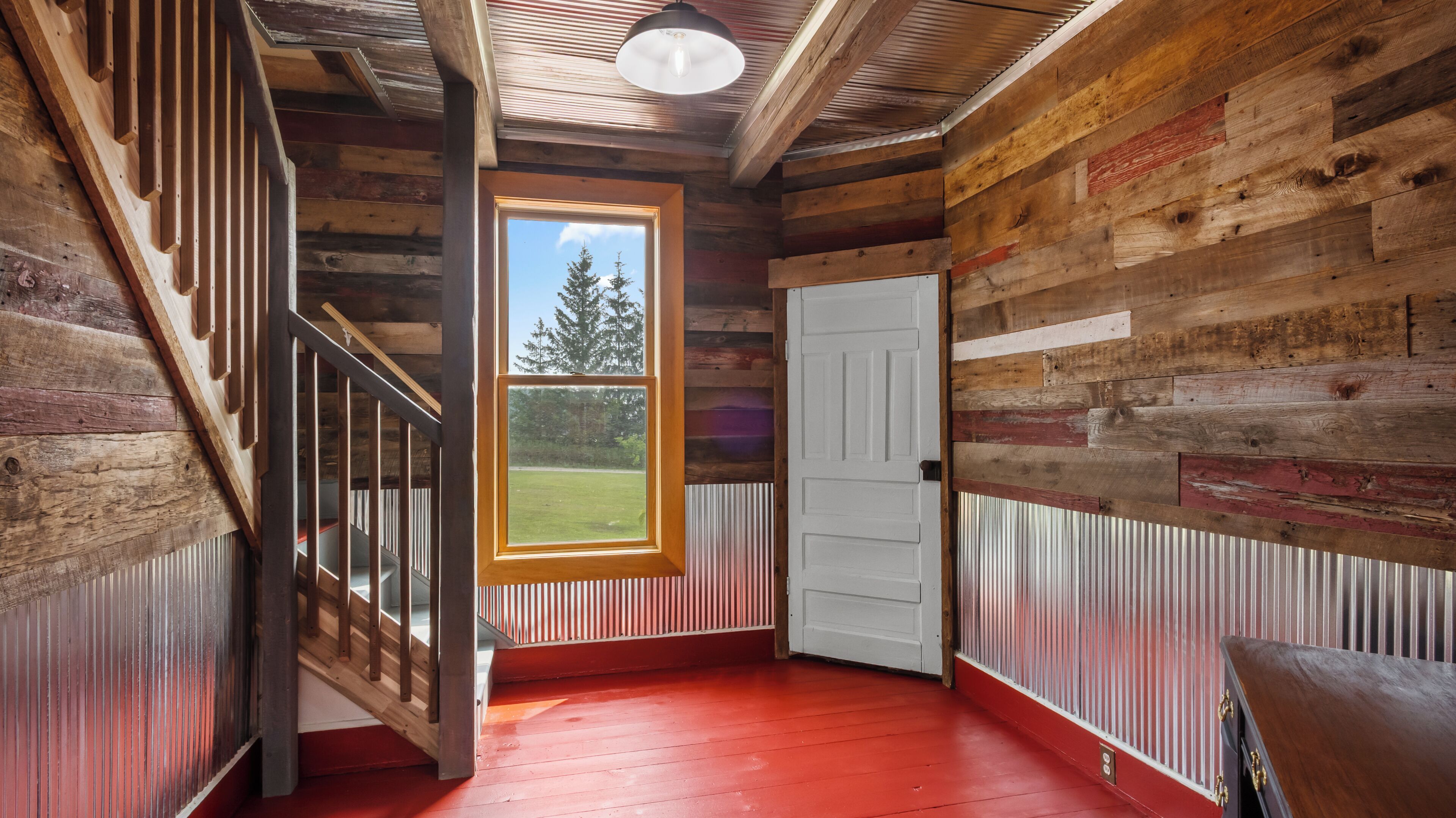 A wooden interior with a red floor, a staircase, and a door leading outside.