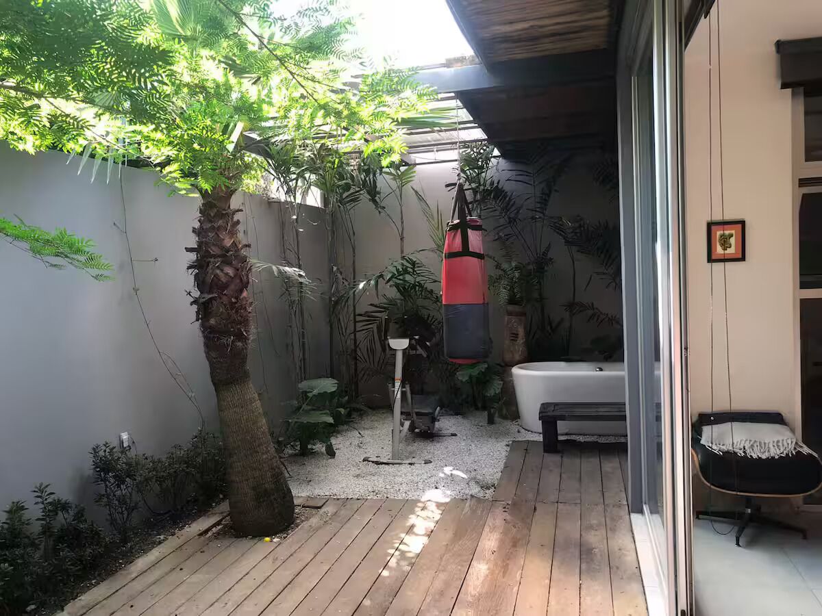Eine Holzterrasse mit einer Palme, einem roten Sandsack und einem schwarzen Massagesessel.