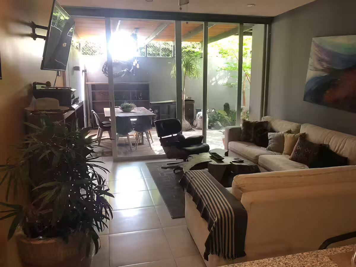 A modern living room with a sofa, a TV, and a dining area with chairs and a table.