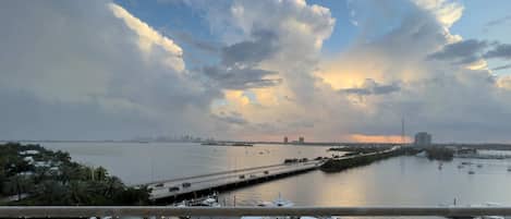 Panoramic balcony view capturing warm golden hour light breaking through dramatic cloud cover over the bay.