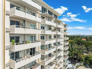 A multi-story building with balconies, large windows, and a view of palm trees and a distant city skyline. - Bahia Serena - Bay Views on Marina With Parking (North Bay Village)