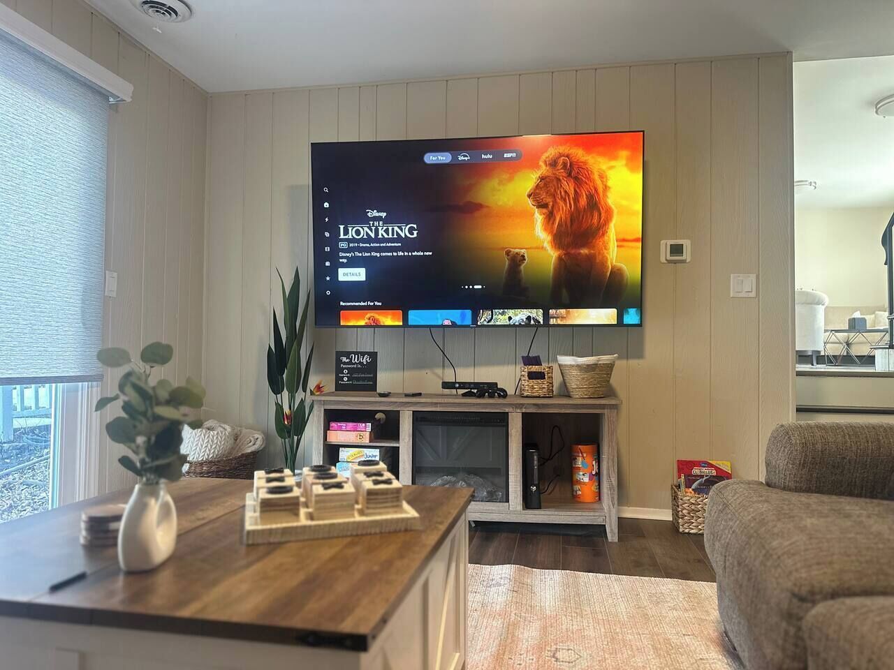 Ein Wohnzimmer mit einem Flachbildfernseher, der 'Der König der Löwen' zeigt, einem Holztisch, einer Pflanze und einem Sofa.