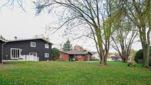 Un quartier résidentiel avec une grande maison noire, une petite maison en bois et une cour verdoyante.