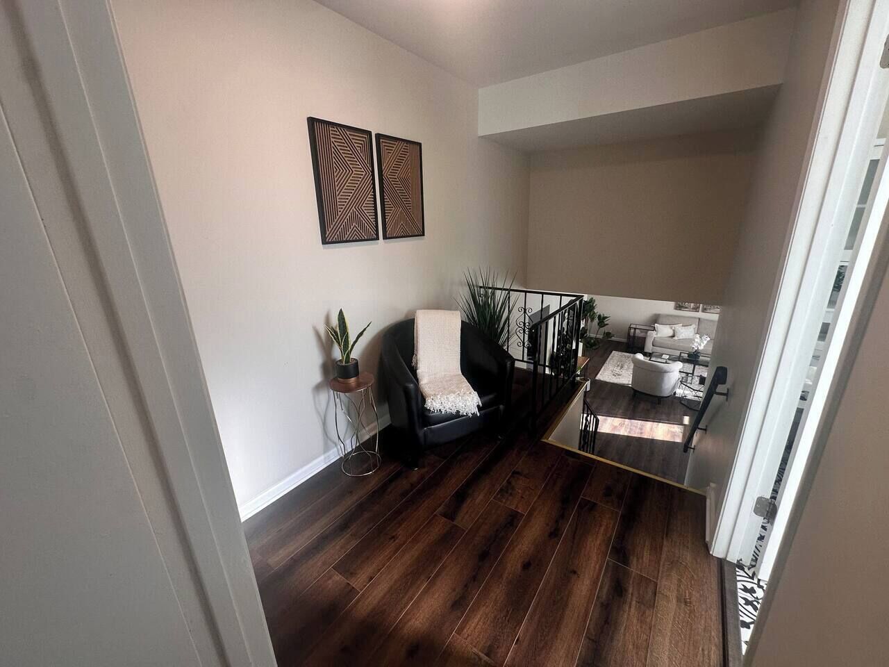 Een modern appartement met een donker houten vloer, een zwarte leren stoel, een kleine potplant en een trap naar een hoger niveau.
