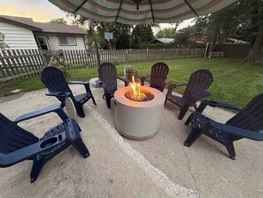 A patio with a circular fire pit and four Adirondack chairs. - Great America Getaway | Sleeps 12 | Near Navy Base (Gurnee)