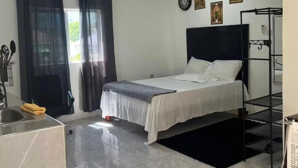 Een slaapkamer met een bed, een raam met gordijnen, een wandklok en een klein plankje met decoratieve objecten.