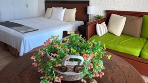 A hotel room with a bed, a green sofa, a wooden coffee table with a floral arrangement, and a lamp. - Cancun Plaza Caribbean Ocean View & Infinity Pool (Cancún)