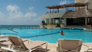 A pool area with lounge chairs, a thatched-roof structure, and a view of the ocean. - Cancun Plaza Caribbean Ocean View & Infinity Pool (Cancún)