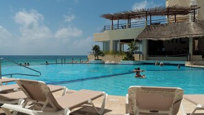 Un espace piscine avec des chaises longues, une structure à toit de chaume et une vue sur l’océan.