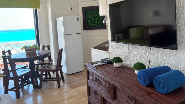 A compact living space with a dining area, kitchenette, and a large flat-screen TV mounted on the wall. - Cancun Plaza Caribbean Ocean View & Infinity Pool (Cancún)