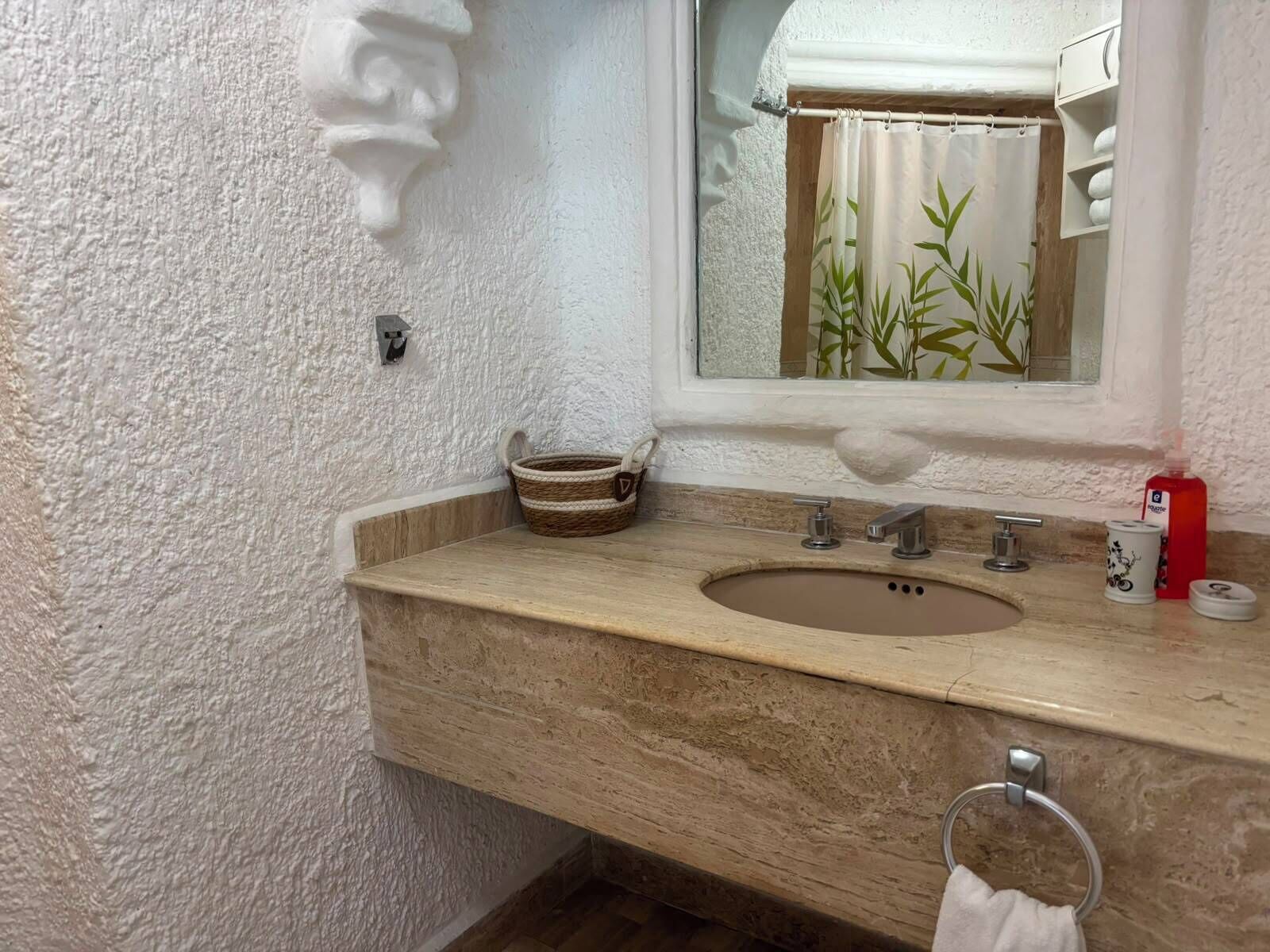 Kylpyhuoneessa on beigenvärinen pesuallas, kaksi hanaa, peili ja pyyheteline.