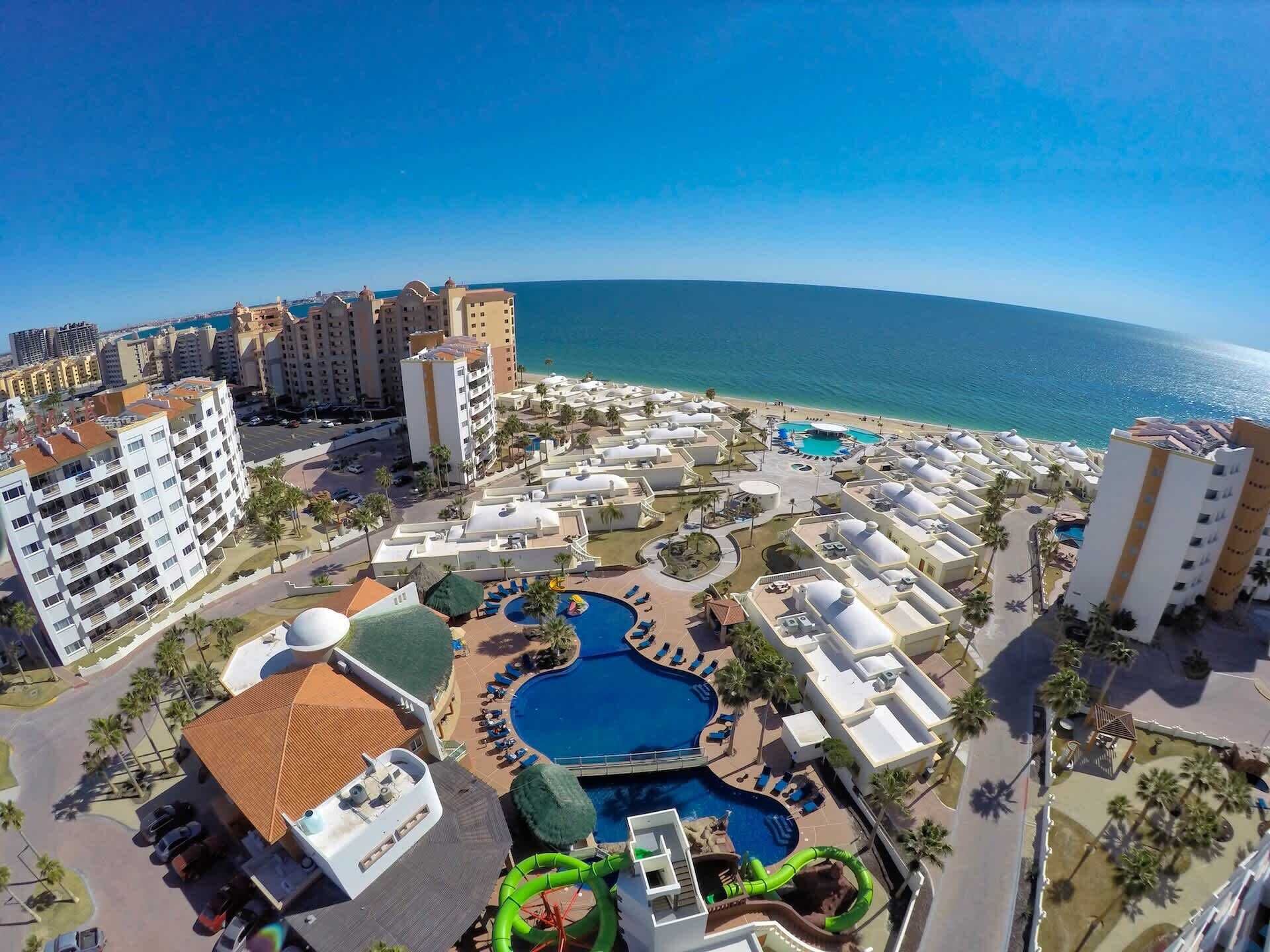 Ein Resort mit mehreren Schwimmbecken, einem Strand und Hochhäusern.
