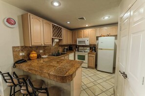 Une cuisine dotée de plans de travail en granit, de meubles en bois, d’un four à micro-ondes, d’un réfrigérateur et d’une horloge murale.