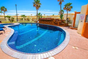Ein Pool mit gefliestem Rand, umgeben von Palmen und einem Gebäude mit gelber Fassade.