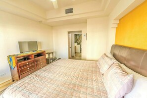 Una camera da letto con un letto, una cassettiera, un televisore e un bagno parzialmente visibile attraverso una porta aperta.