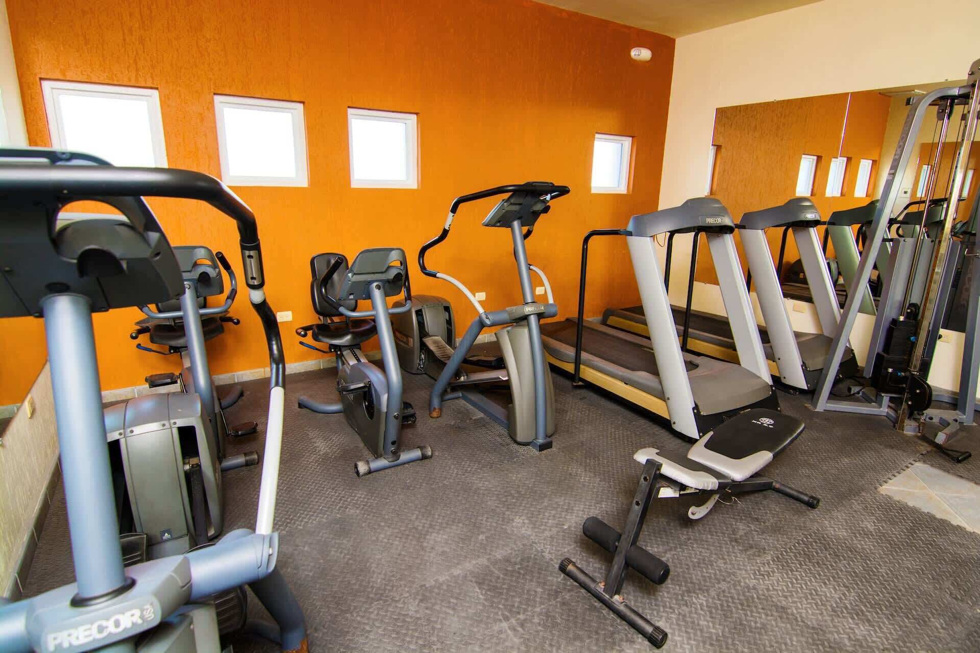 Ein Fitnessstudio mit verschiedenen Trainingsgeräten, darunter Laufbänder, Crosstrainer und Kraftgeräte.
