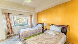 Quarto de hotel com duas camas, janela com cortinas, ventilador de teto e vista para o exterior.