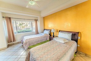 Ein Hotelzimmer mit zwei Betten, einem fensterbelaubten Fenster, einem Deckenventilator und Blick ins Freie.