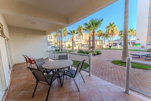 Un balcon avec une table ronde et des chaises, donnant sur un espace pavé agrémenté de palmiers et de bâtiments.