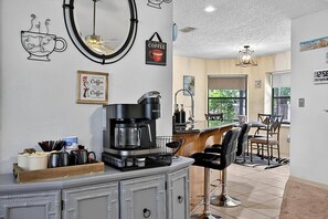 A kitchen with a coffee maker, bar stools, and a dining area with a view. - Breezy Palm | Private Pool | Minutes to Beach and Golf | Palm Coast (Palm Coast)