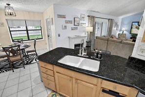 A modern kitchen with a black granite countertop, wooden cabinets, and a double sink. - Breezy Palm | Private Pool | Minutes to Beach and Golf | Palm Coast (Palm Coast)
