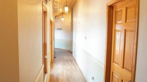 Un corridoio con pavimento in legno e porte, che conduce a una stanza con ventola a soffitto e un lampadario.