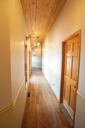 A hallway with wooden floors and doors, leading to a room with a ceiling fan and a light fixture. - Second Heaven Lodge Southern Iowa Escape (Moulton)
