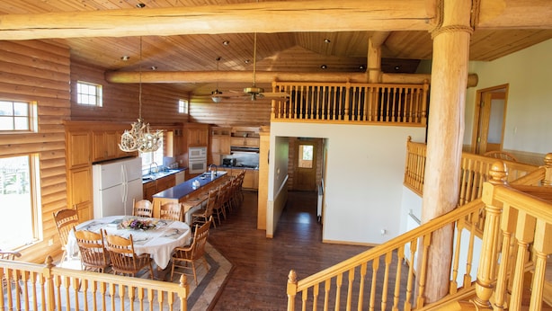 Un ampio interno di una baita in legno con zona pranzo, cucina e una scala che conduce a un piano superiore.