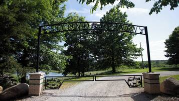 A metal gate with a deer silhouette, a brick structure, and a gravel path leading to a body of water.