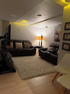 A living room with two leather sofas, a white rug, a flat-screen TV, a lamp, and framed pictures on the wall.
