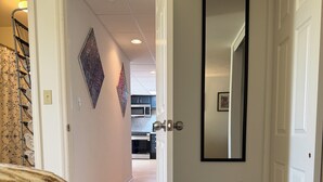 A hallway with a bed, a door with a mirror, and a kitchen in the background. - Serene 2-bedroom private basement in charming Wentzville (Wentzville)