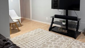 A living room with a flat-screen TV on a black stand, a white chair, a white rug, and a wooden floor. - Serene 2-bedroom private basement in charming Wentzville (Wentzville)