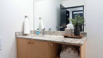 A bathroom with a granite countertop, a sink, a mirror, and a wooden cabinet with towels.