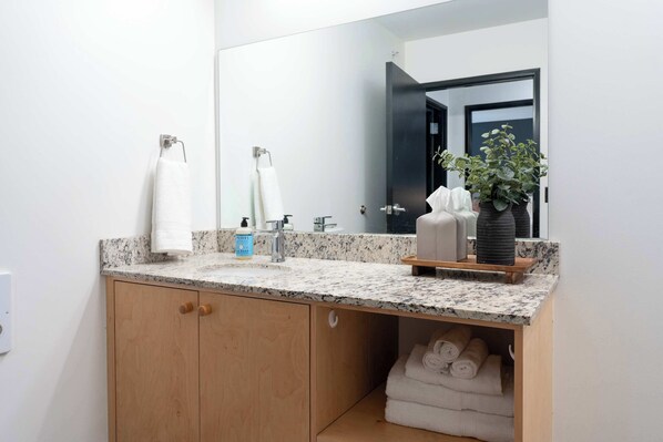 A bathroom with a granite countertop, a sink, a mirror, and a wooden cabinet with towels.