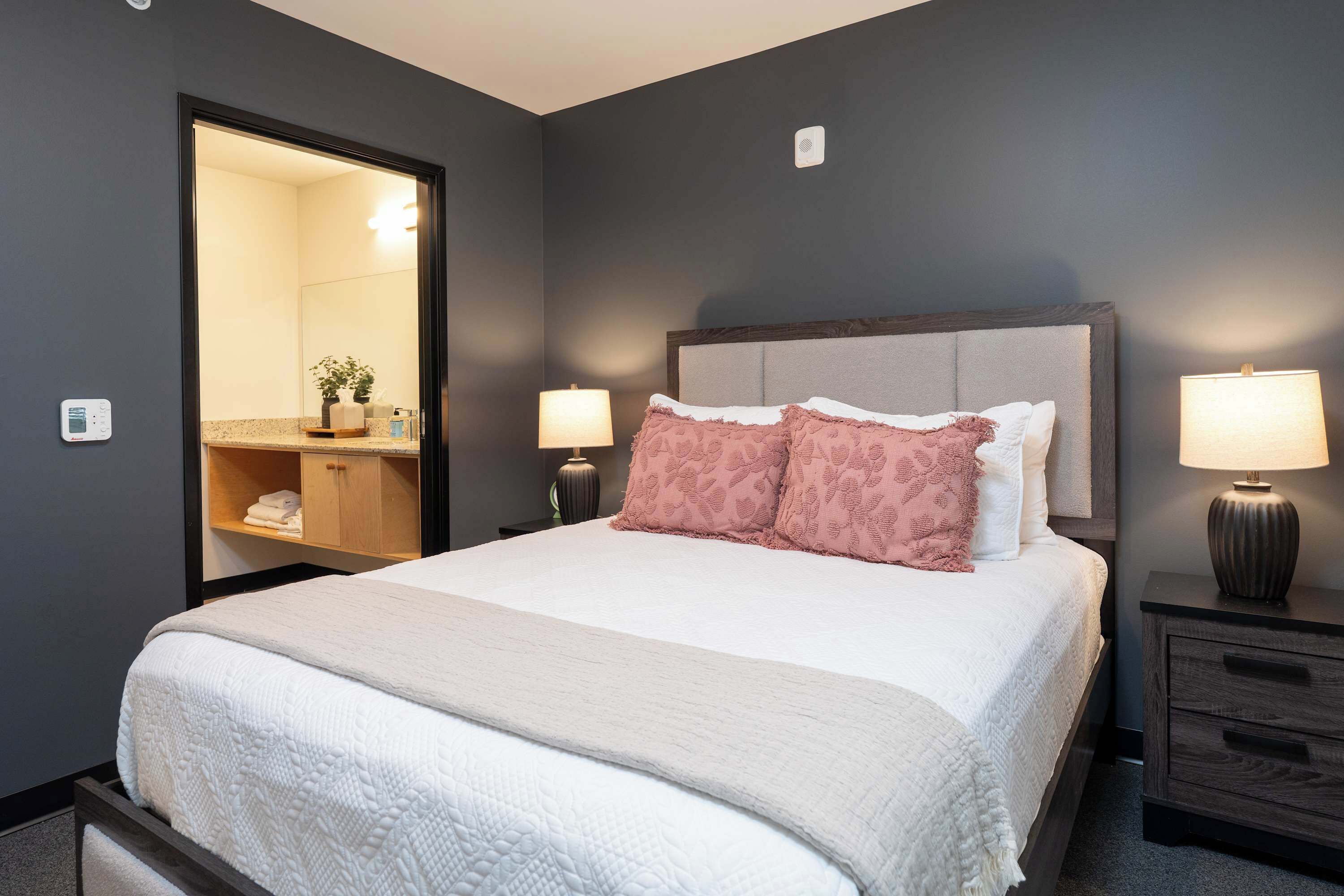A neatly made bed with a headboard, two bedside lamps, a nightstand, and a mirror.