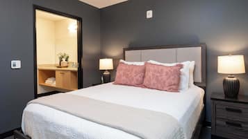 A neatly made bed with a headboard, two bedside lamps, a nightstand, and a mirror.