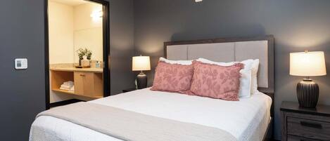 A neatly made bed with a headboard, two bedside lamps, a nightstand, and a mirror.