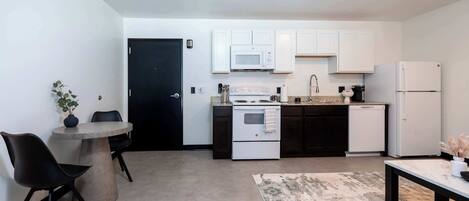 A compact kitchen with white cabinets, a microwave, a stove, and a refrigerator.