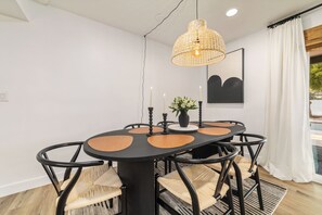 Ein Essbereich mit einem runden Tisch, schwarzen Stühlen, einer gewebten Pendelleuchte, Kerzen und einem gerahmten Kunstwerk an der Wand.