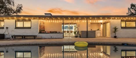 Una casa con piscina, luces colgantes y un mural con motivos desérticos.
