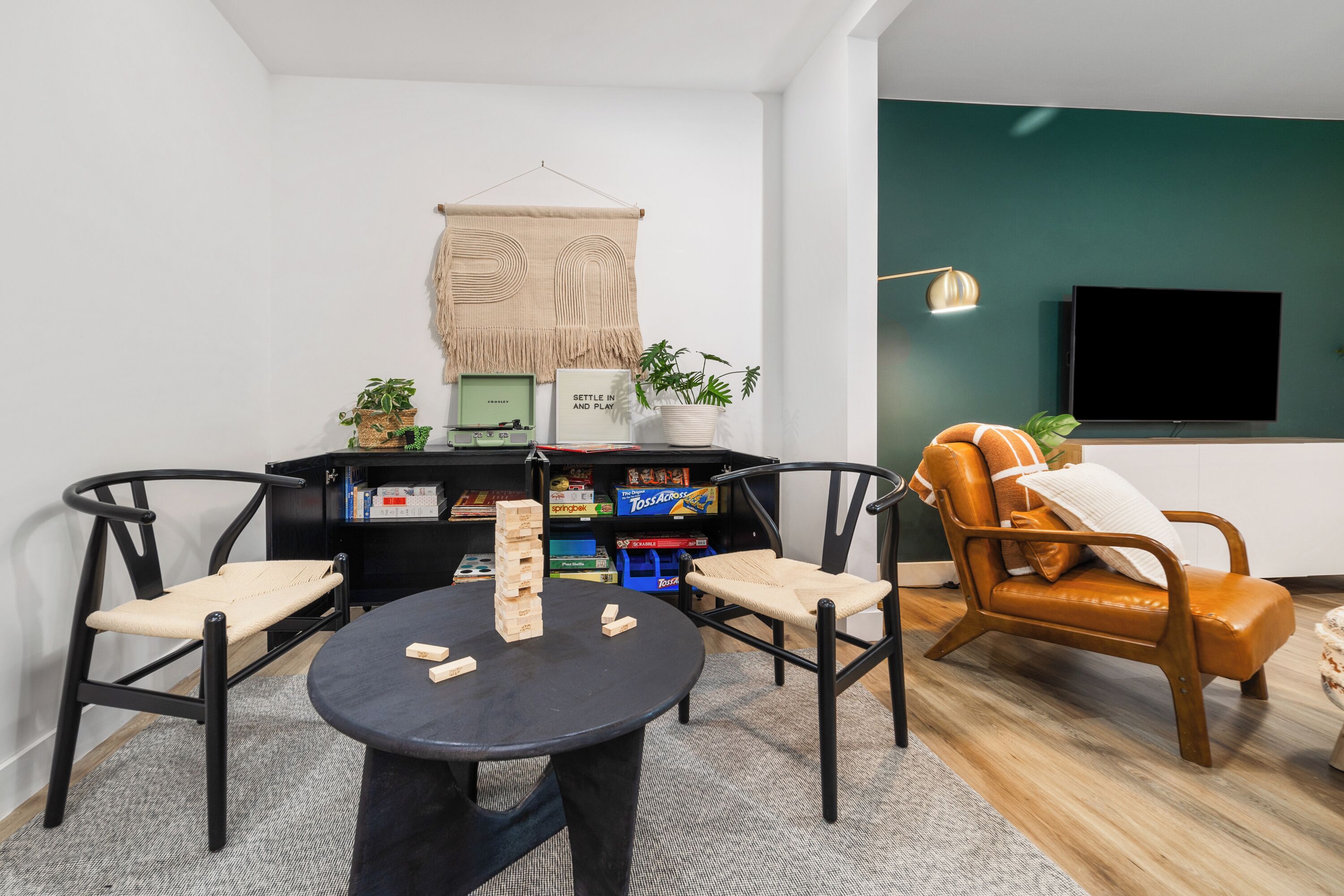 Ein modernes Wohnzimmer mit einem runden Tisch, zwei Stühlen, einem Bücherregal, einem Fernseher und einer Wand in Grünton.
