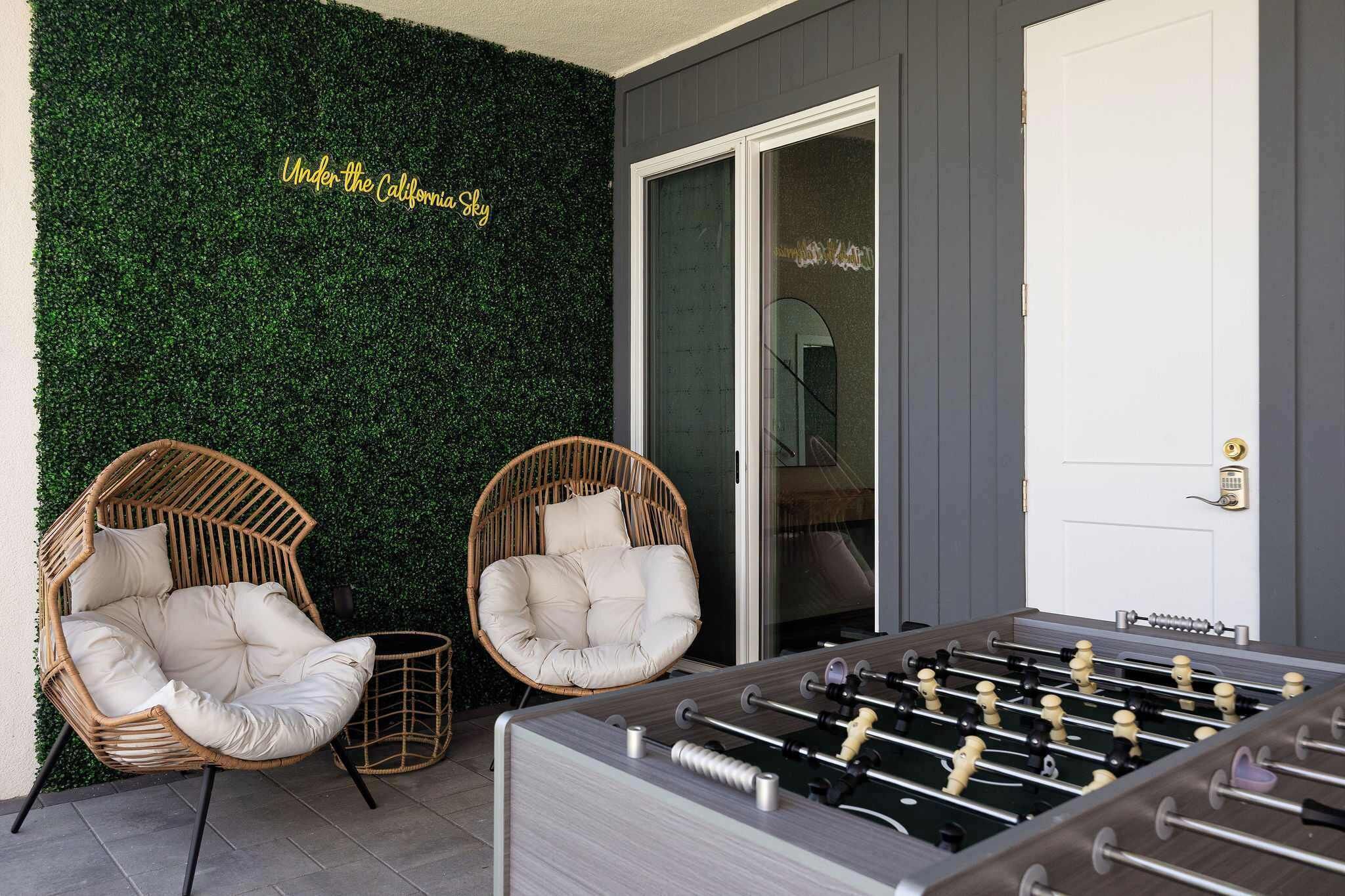 Una habitación con una pared verde, dos sillas de mimbre, una mesa de fútbol de mesa y una puerta corrediza de vidrio.