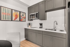 Cuina moderna amb armaris grisos, microones, cafetera i un vàter.