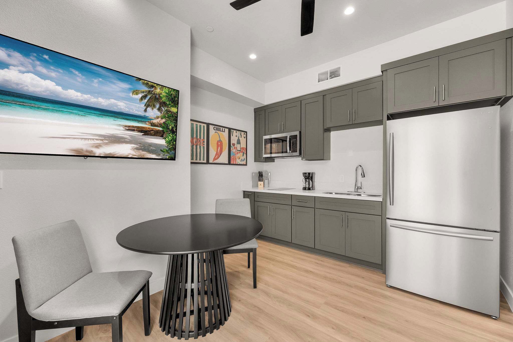A modern kitchen with grey cabinets, a stainless steel refrigerator, and a dining area with a round table and chairs.