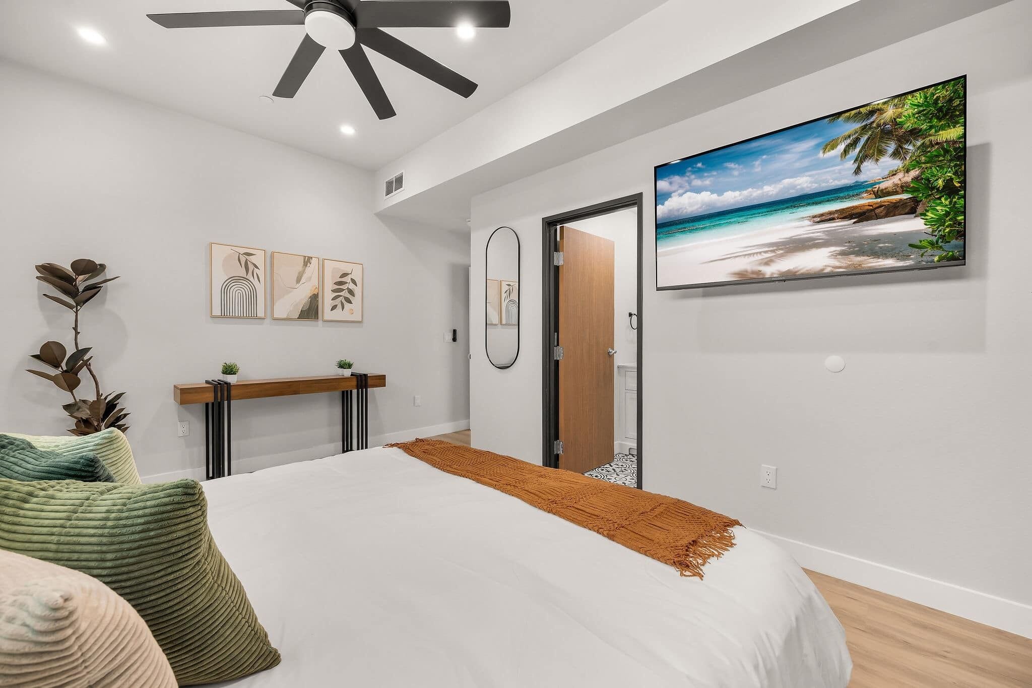A bedroom with a bed, a ceiling fan, a TV, and artwork on the wall.